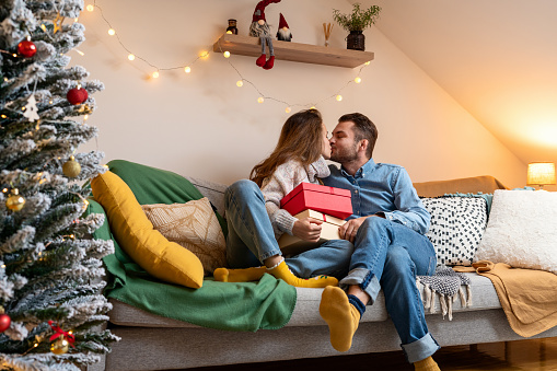 Young married couple giving each other Christmas gifts and kissing. Christmas holidays.