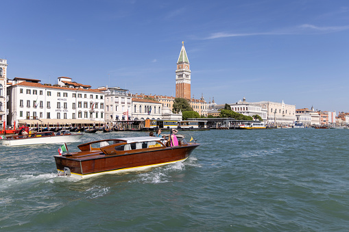 Venice, Italy - September 27, 2023: Grand Canal, historic decorative tenement houses by the water, tourists on boats and gondolas explore the city. St Mark's Campanile in a distance