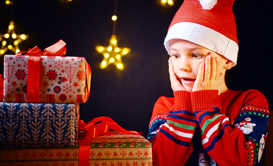 The boy in the cap is surprised by the number of gifts for Christmas or New year. Happy children's emotions.