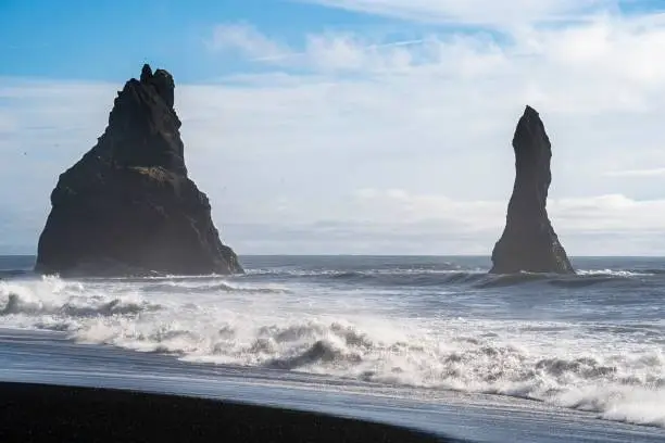 An idyllic black sand beach in Iceland with two prominent basalt towers rising from the ocean