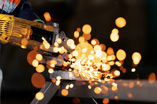 Craftsmanship in an industrial workshop. Dance of sparks bokeh and steel, a skilled craftsperson operates a grinder, grinding steel with a level of precision. Sparks like fiery comets, explode forth, illuminating the intricate work. Using the grinder to smooth the surface of steel.