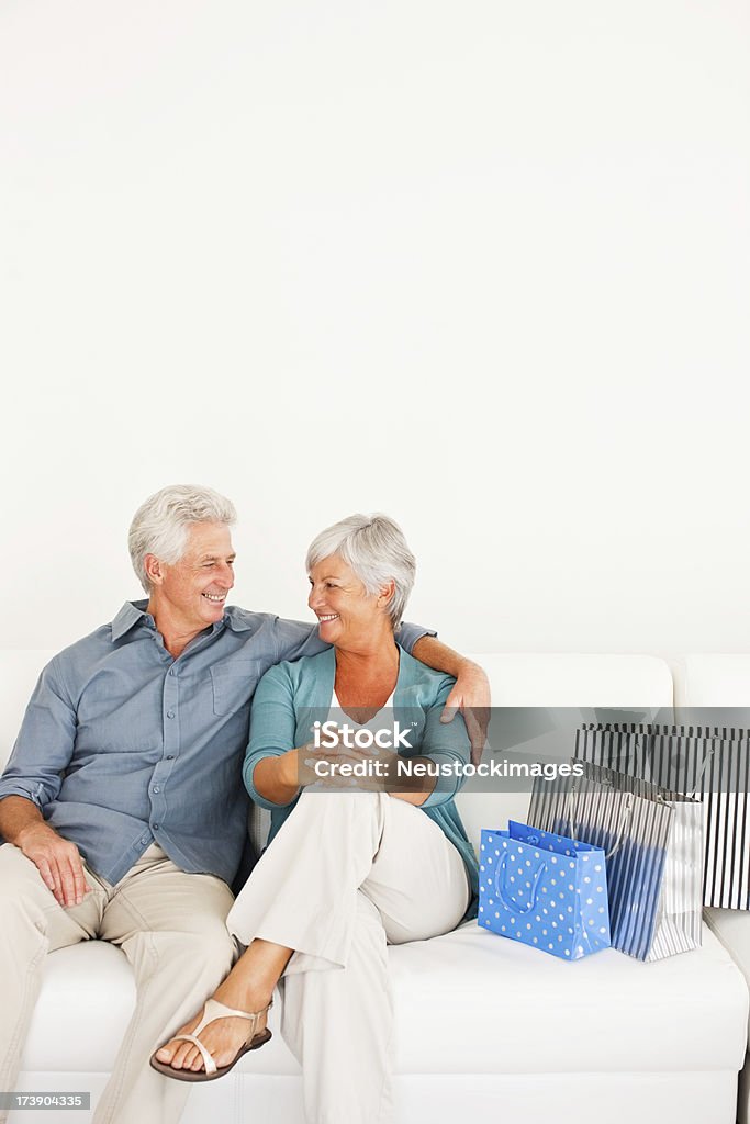 Felice coppia senior seduto sul divano con borse shopping - Foto stock royalty-free di 60-64 anni