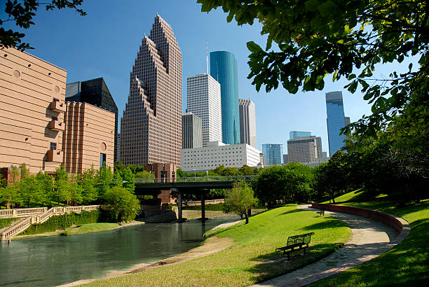 Modern skyscrapers in downtown Houston behind park with lake Modern skyscrapers of Houston, Texas are seen in this horizontal color image across a waterway flowing through a city park.  A perfect, clear blue sky is a backdrop to this afternoon cityscape.  Tops of the buildings are somewhat outlined by tree branches.  A park bench and walking trail are included in the foreground. houston texas stock pictures, royalty-free photos & images