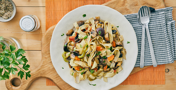 Healthy organic Italian vegetable Tagliatelle pasta, made from mushrooms, zucchini, Spanish onion, garlic, served on a modern ceramic plate, on a light wooden kitchen or restaurant table, representing a healthy lifestyle, body care and wellbeing, table top view with a copy space
