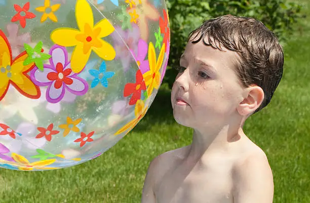 Little boy stares at a large beachball he's tossing into the air. Eyes focused. Ball shows slight movement.