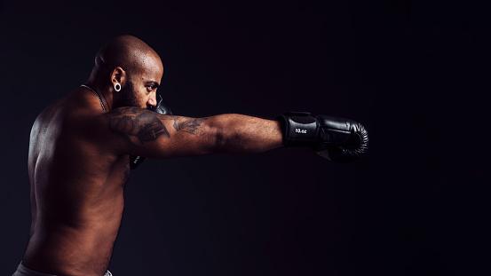 Mixed-race man throwing a cross into the air on a black background with boxing gloves