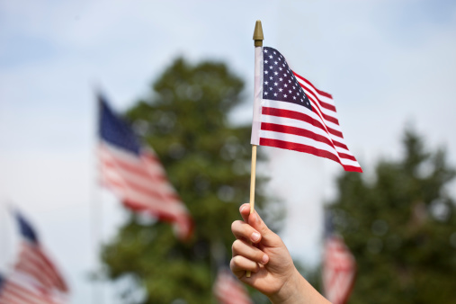 Photo of a child's hand holding up a small United States flag during a memorial service