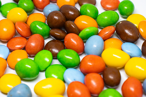 Colorful chocolate M&Ms in and out of focus on white background.