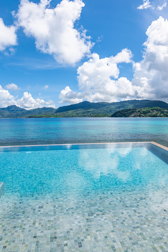 Vertical image with mosaic tiles infinity pool overlooking sea and mountains of Seychelles Island. Blue sky and clouds. Travel image.