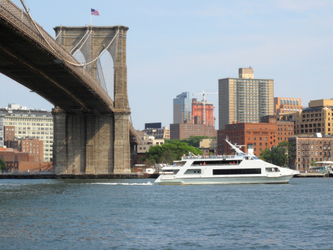 A ferry goes under the Brooklyn Bridge on a sunny day.