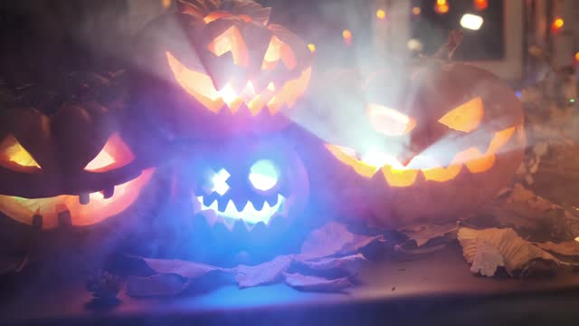 Festive traditional carved pumpkins with glowing lanterns inside flashing colorful lights  in thick smoke
