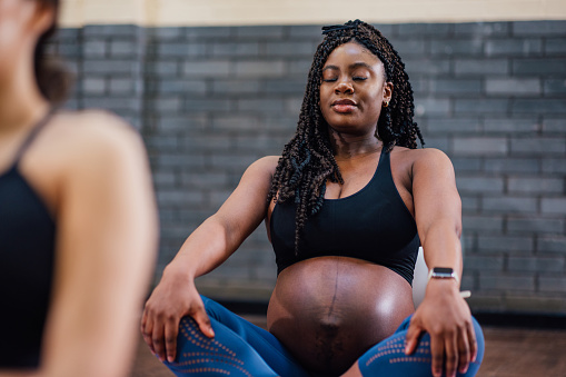 A group of pregnant mothers-to-be taking part in a yoga class in a community centre in Seaton Delaval, North East England. The main focus is one woman sitting crossed legged on the floor with her eyes closed and doing breathing exercises to help with pregnancy and birthing.