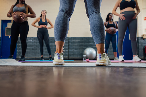 A low angle view of a group of pregnant mothers-to-be taking part in a yoga class in a community centre in Seaton Delaval, North East England. They are using yoga mats and are following the instructor at the front of the class who is out of shot while holding onto their stomachs, doing breathing techniques to help with birthing and pregnancy.