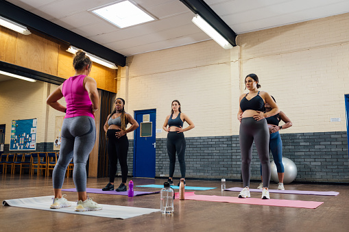 A group of pregnant mothers-to-be taking part in a yoga class in a community centre in Seaton Delaval, North East England. They are using yoga mats and are following the instructor at the front of the class while holding onto their stomachs, doing a yoga position to help with birthing and pregnancy.