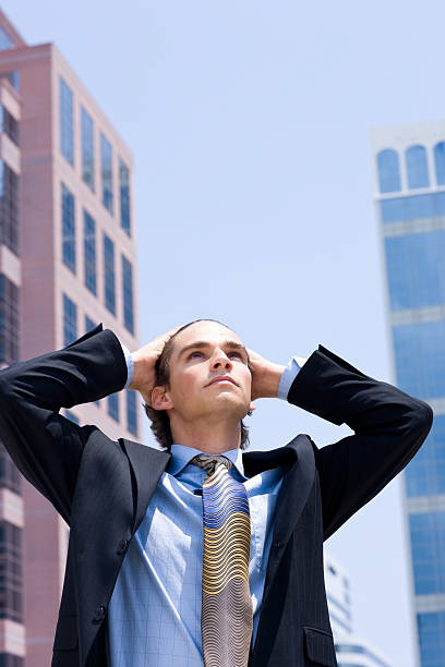 istock Young businessman surrounded by tall buildings looking up 173909230