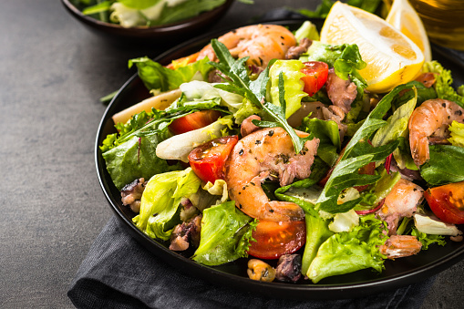 Seafood salad with fresh leaves tomatoes and fried seafood at black stone table.