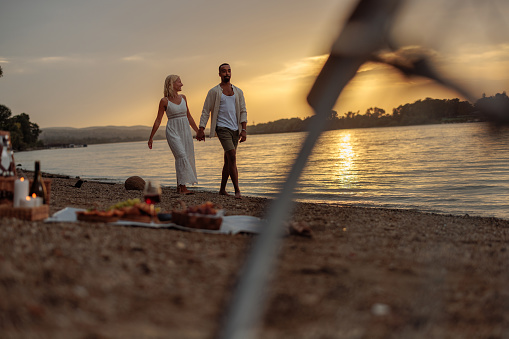 couple slow walking by the river while having a picnic during sunset, looking happy and in love