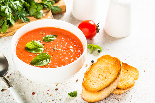 Tomato soup with basil at white table. Summer cold vegan dish.