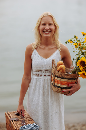 Beautiful portrait showing an albino caucasian girl carrying picnic box and sunflowers while smiling by the river