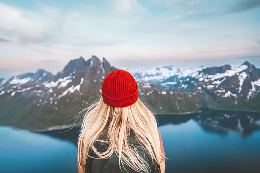 Traveler woman hiking outdoor in Norway travel adventure vacations healthy lifestyle blonde hair girl hiker in red hat with backpack enjoying mountains view