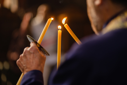 Close-up of priest's hands lighting candles in church