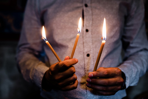 Close-up of man's hands holding burning candles in church. Religion concept