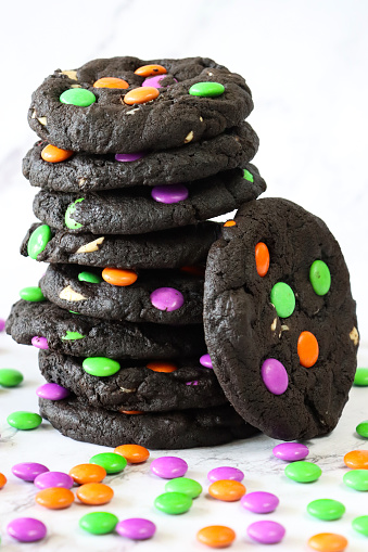 Stock photo showing close-up view of pile of Halloween white chocolate chip, black cocoa biscuits decorated with crunchy sugar coated, multicoloured chocolate sweets. Home baking concept photo.