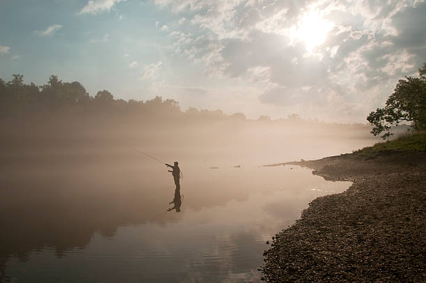 Colorful sunrise and fishing on the river bank. Silhouette of a man with a fishing rod in motion. Belarusian morning landscape on the Pripyat river.