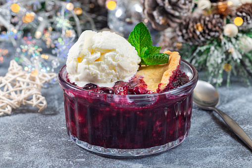 Berry cobbler in glass ramekin with ice cream, Christmas decoration with bokeh on background, horizontal