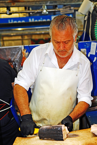 Fishmonger cleaning with a knife a fresh sea bass on his stall at the Central Ataranzas food market in Malaga.