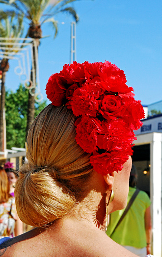 Young woman wearing an awesome hairstyles with fresh roses on her hair for the Flamenco festivities that take place every year in May during the local holidays in Jerez de la Frontera.