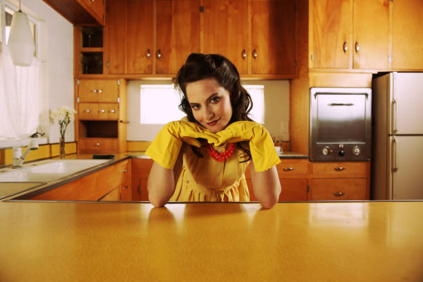 Fifties Housewife in Kitchen "Beautiful fifties housewife in fifties-style vintage kitchen, leaning on golden formica counter top and wearing yellow rubber gloves.Slight cross-processing applied to achieve vintage photo effect.More with this model:" retro 1950s kitchen stock pictures, royalty-free photos & images