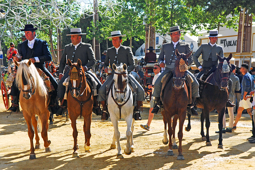 Group of five andalusian horse riders parading with their purebred horses at the promenade of the flamenco fair that takes place every year in Jerez de la Frontera during their local festivities.