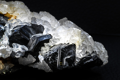 A crystal and stone cluster with clear white quartz, silver metallic pyrite and black tourmaline surrounded by matrix macro close up isolated on a black surface background