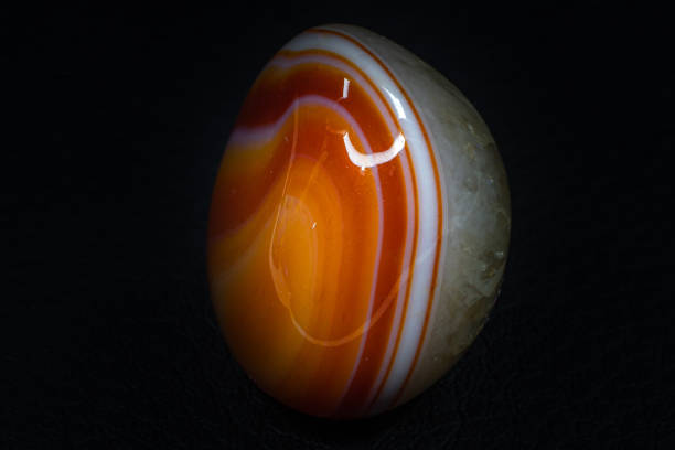 Clear quartz on vibrant orange and white banded carnelian agate chalcedony tumbled crystal macro isolated on a black leather background