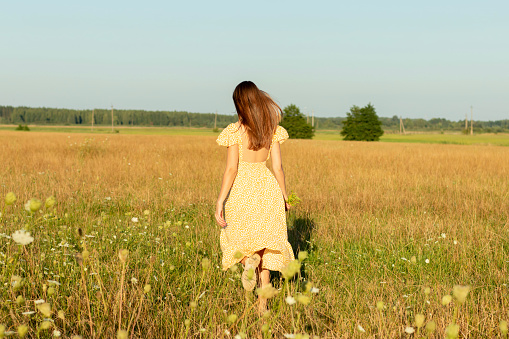 Young beautiful woman in yellow dress closeup with yellow field flowers in hand on the natural background in summertime.