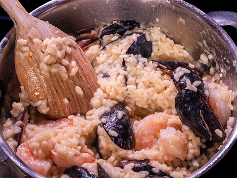 Creating a delectable Italian seafood risotto with saffron-infused rice in a pot using a wooden spoon.
