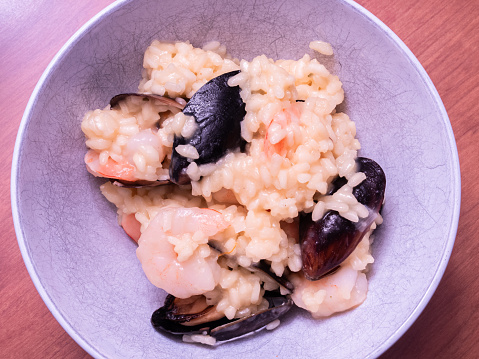 Italian seafood risotto, rich and creamy, adorned with mussels, shrimp, and saffron-infused rice, presented in a white bowl resting on a wooden board.