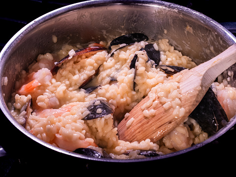 Creating a delectable Italian seafood risotto with saffron-infused rice in a pot using a wooden spoon.