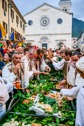 Gualdo Tadino, Umbria, Italy, September 22 -- A scene of celebration with typical food during a medieval reenactment in the main square of the town of Gualdo Tadino in Umbria, central Italy. The Umbria region, considered the green lung of Italy for its wooded mountains, is characterized by a perfect integration between nature and the presence of man, in a context of environmental sustainability and healthy life. In addition to its immense artistic and historical and medieval heritage, Umbria is famous for its food and wine production and for the high quality of the olive oil produced in these lands. Image in high definition quality.