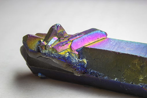 Titanium aura quartz double terminated point with a small cluster, altered natural quartz with strong rainbow color close up on white background.