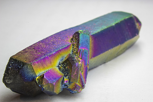 Titanium aura quartz double terminated point with a small cluster, altered natural quartz with strong rainbow color close up on white background.