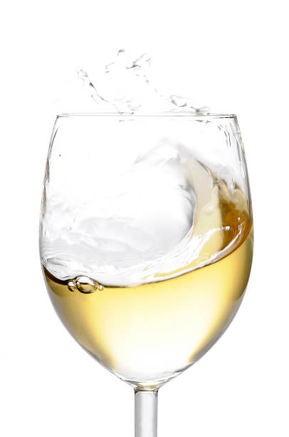 White wine pops up to the top of the glass. White background. Studio shot in motion.