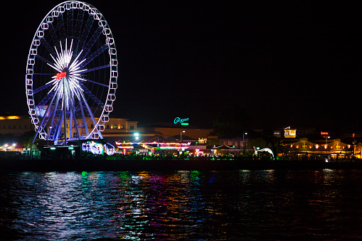 Illuminated Asiatique The Riverfront with ferris wheel in Bangkok seated in Bang Kho Laem at night seen from boat on Chao Praya river. Riverfront complex and promenade are offering many restaurants