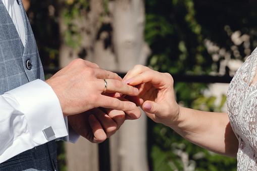 Close-up of bride's hands putting wedding ring on groom's finger.