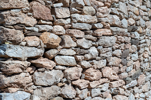 Rocky empty wall construction background texture. Old rough solid multicolor stonewall, blank masonry for backdrop, sunny day. Copy space.