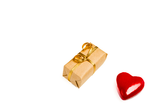 Gift box wrapped in brown paper over white background and a red object in heart shape over white background.Conceptual image for Valentine's day -holiday. Image shoo.t in studio