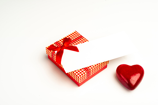 View of red gift box with ribbon an object in heart shape over white background isolated.IMAGE MADE IN STUDIO AS CONCEPTUAL IMAGE FOR VALENTINE'S DAY