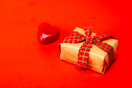 View of red gift box with ribbon an object in heart shape over red color background isolated.IMAGE MADE IN STUDIO AS CONCEPTUAL IMAGE FOR VALENTINE'S DAY