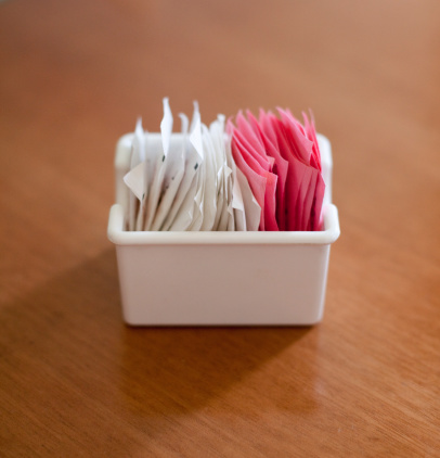 A container of sweetener and sugar packets on a table.